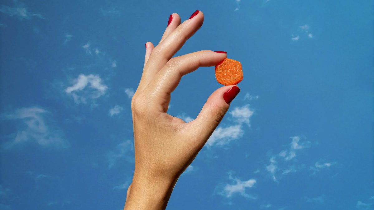 Female model hand holding gummy supplement on a blue-sky background
